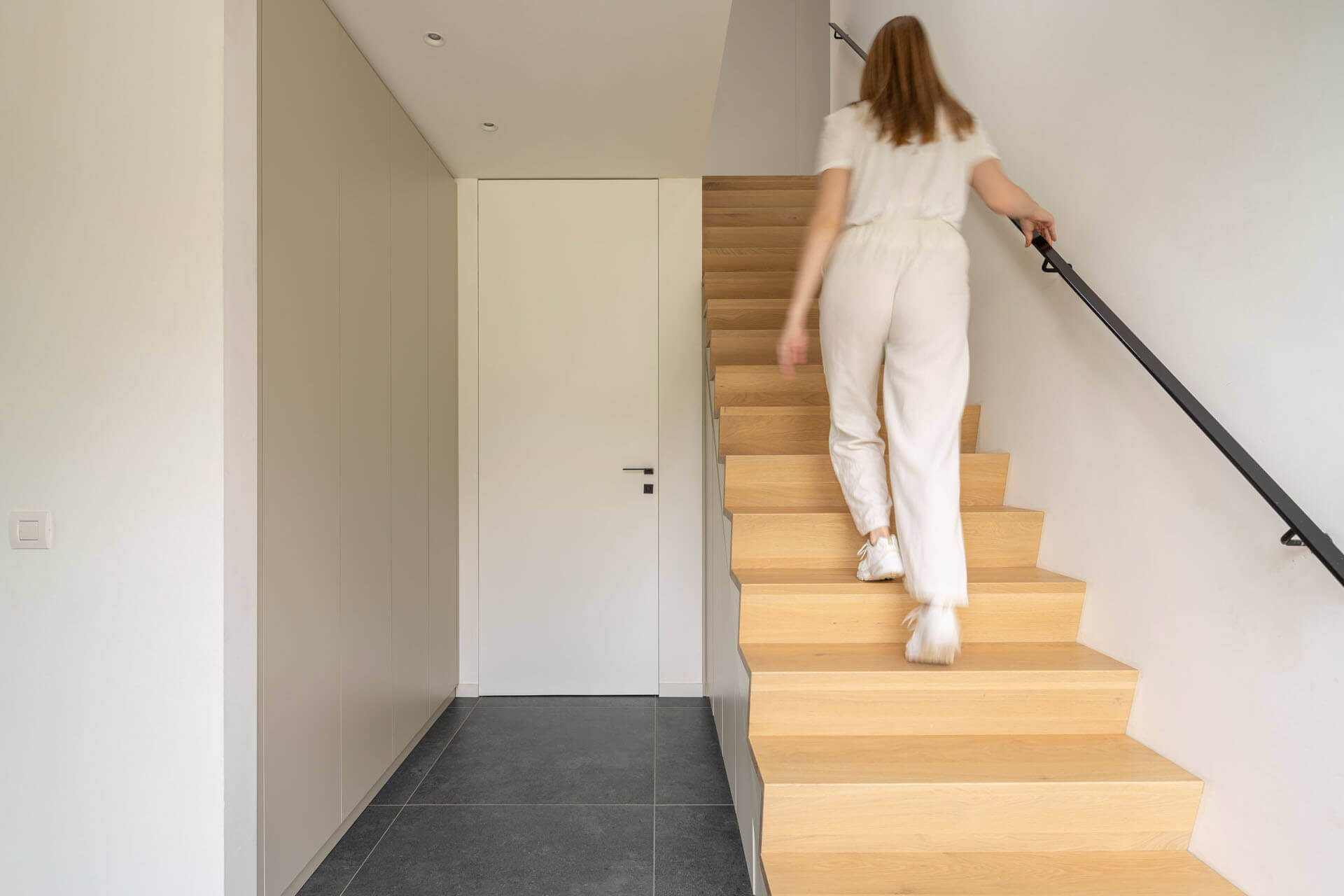 Femme montant les escaliers dans un hall avec une armoire sous escalier sur mesure