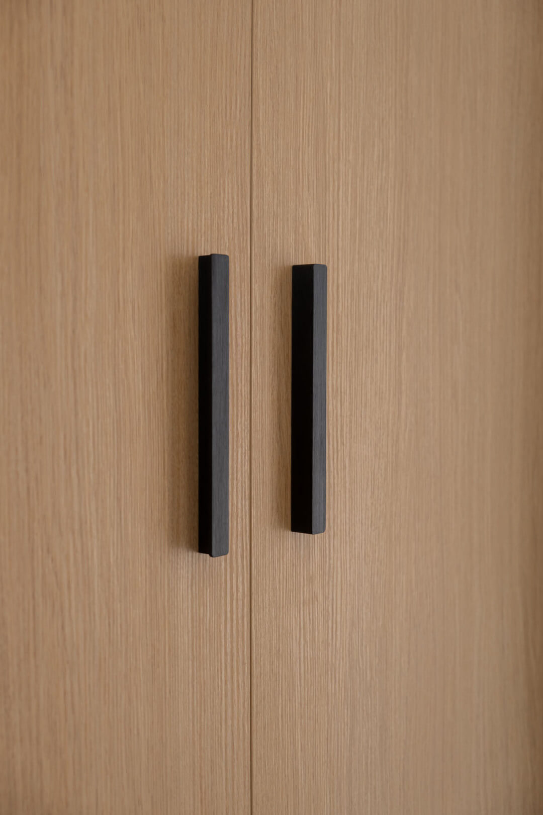 Gros plan sur une poignée noire mate d'une porte de placard en chêne naturel.