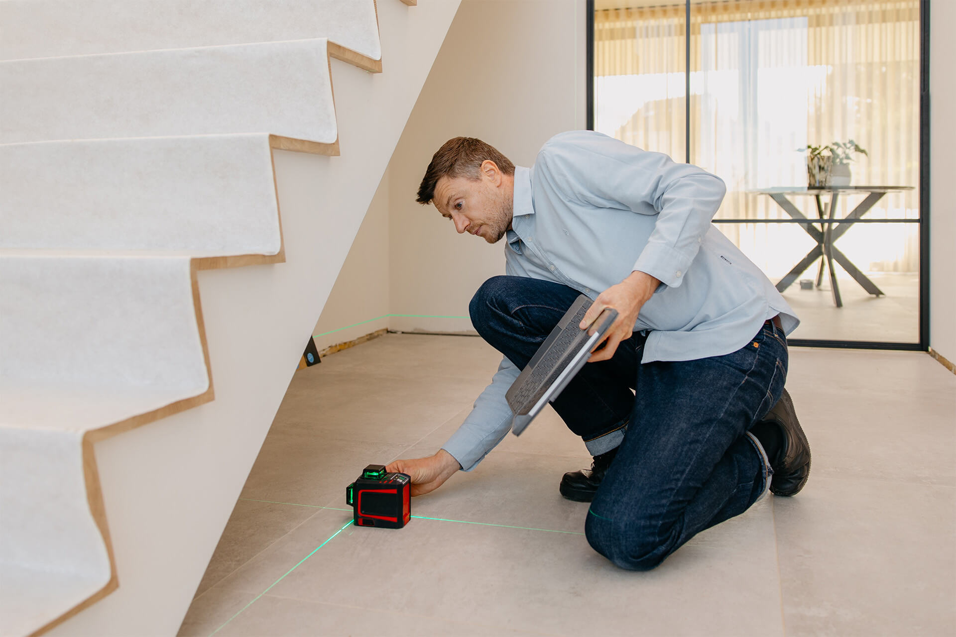 Un homme du service d'arpentage mesure l'espace sous les escaliers pour y installer une armoire sur mesure.