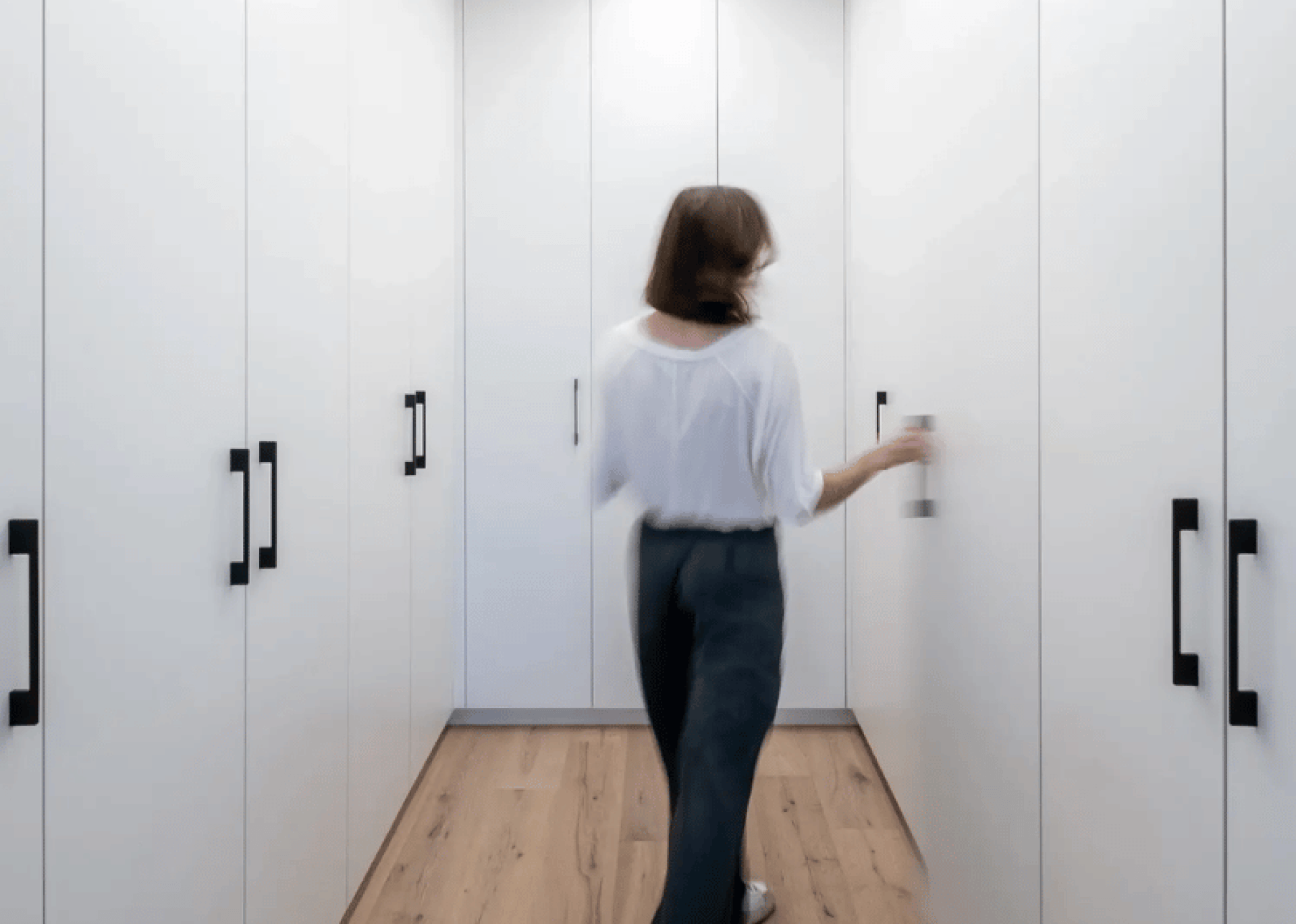 Deux placards en forme de U, situés dans les angles, forment un dressing à l'avant, blanc.