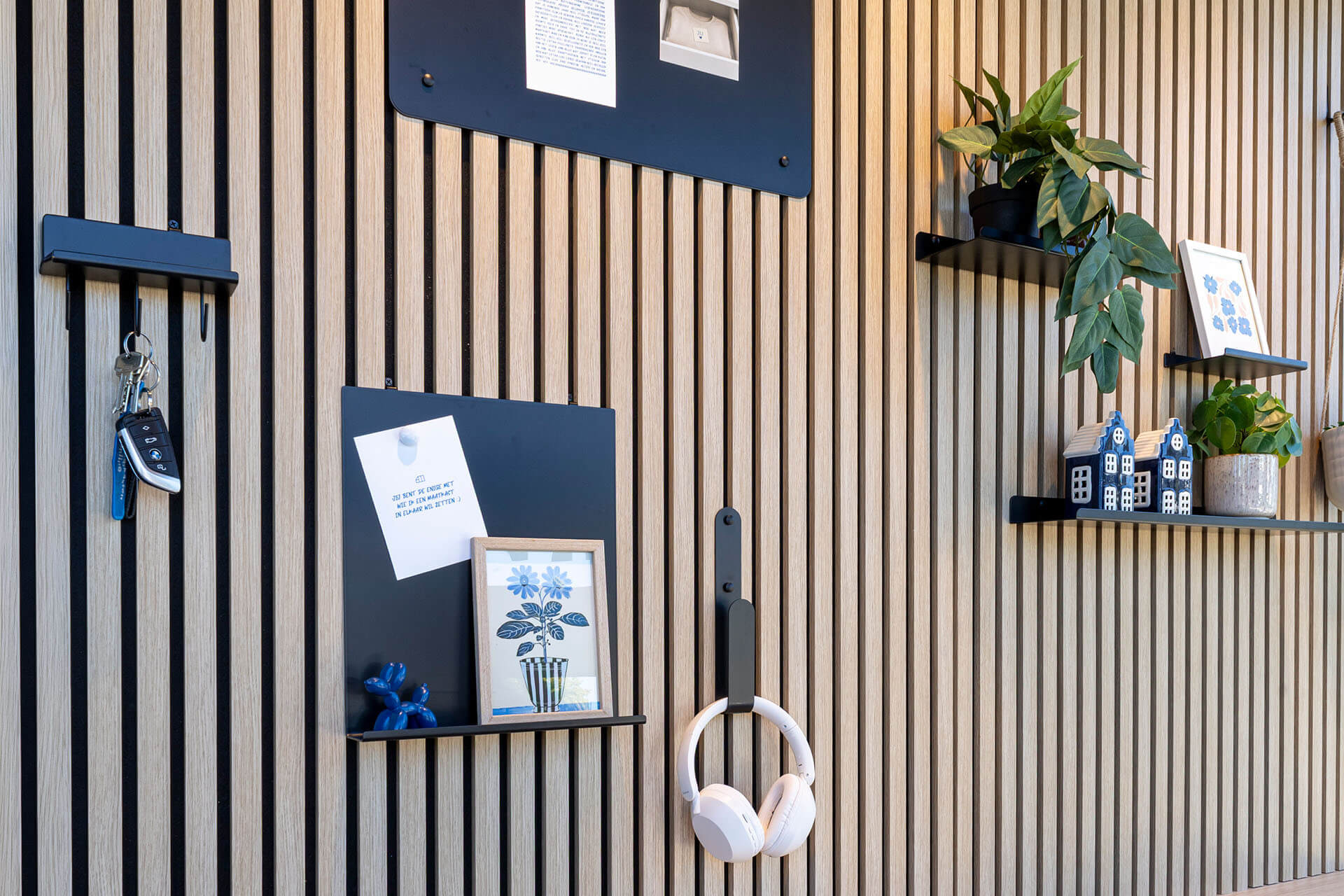 Un mur recouvert de panneaux acoustiques et d'accessoires tels qu'un tableau magnétique, des étagères murales et des crochets pratiques. 