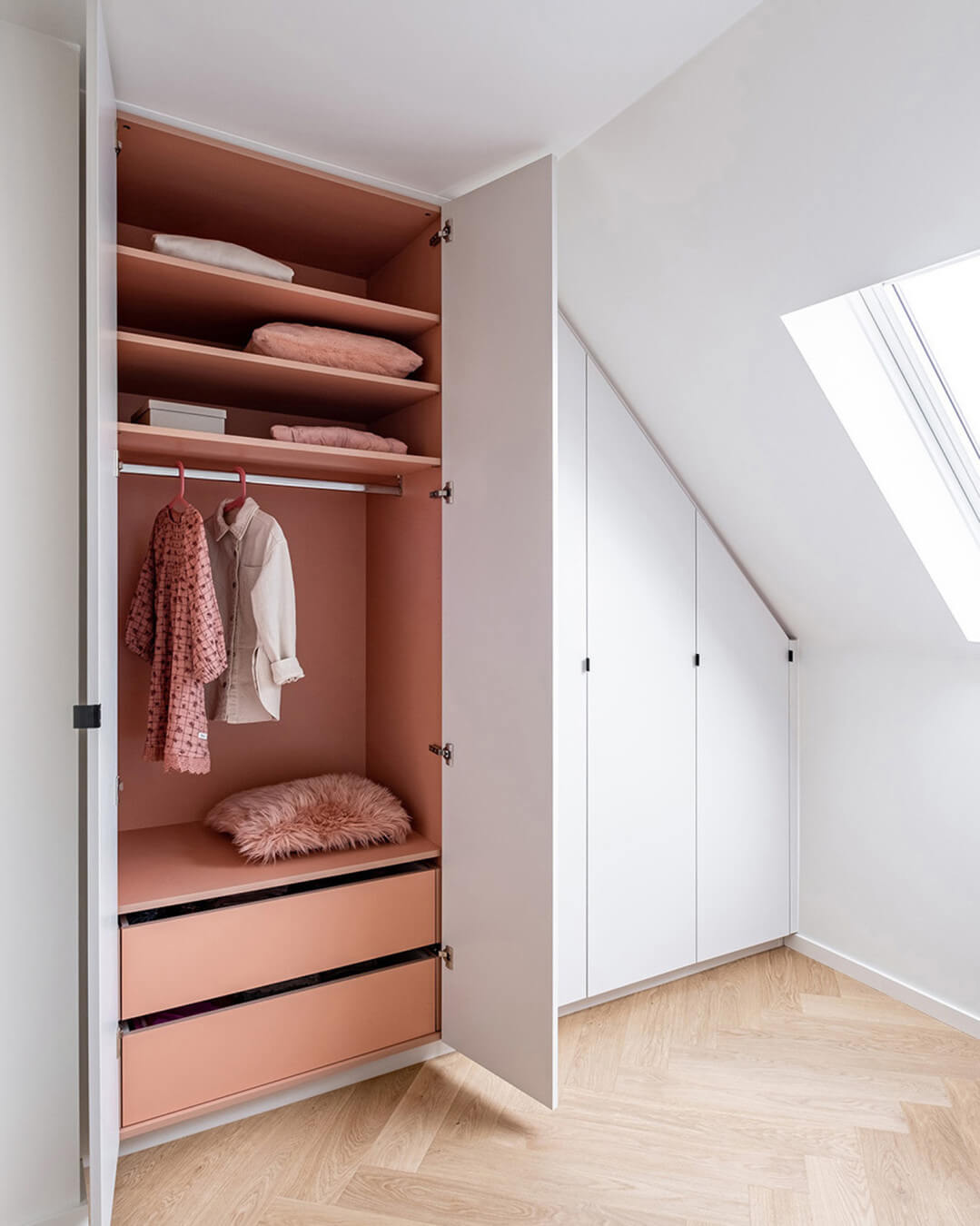 Armoire sur mesure sous un toit en pente avec une couleur intérieure rose.