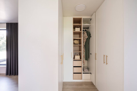 Un meuble d'angle en forme de U, couleur Blanc cassé, avec des poignées en laiton à motif diamant, dans une chambre.