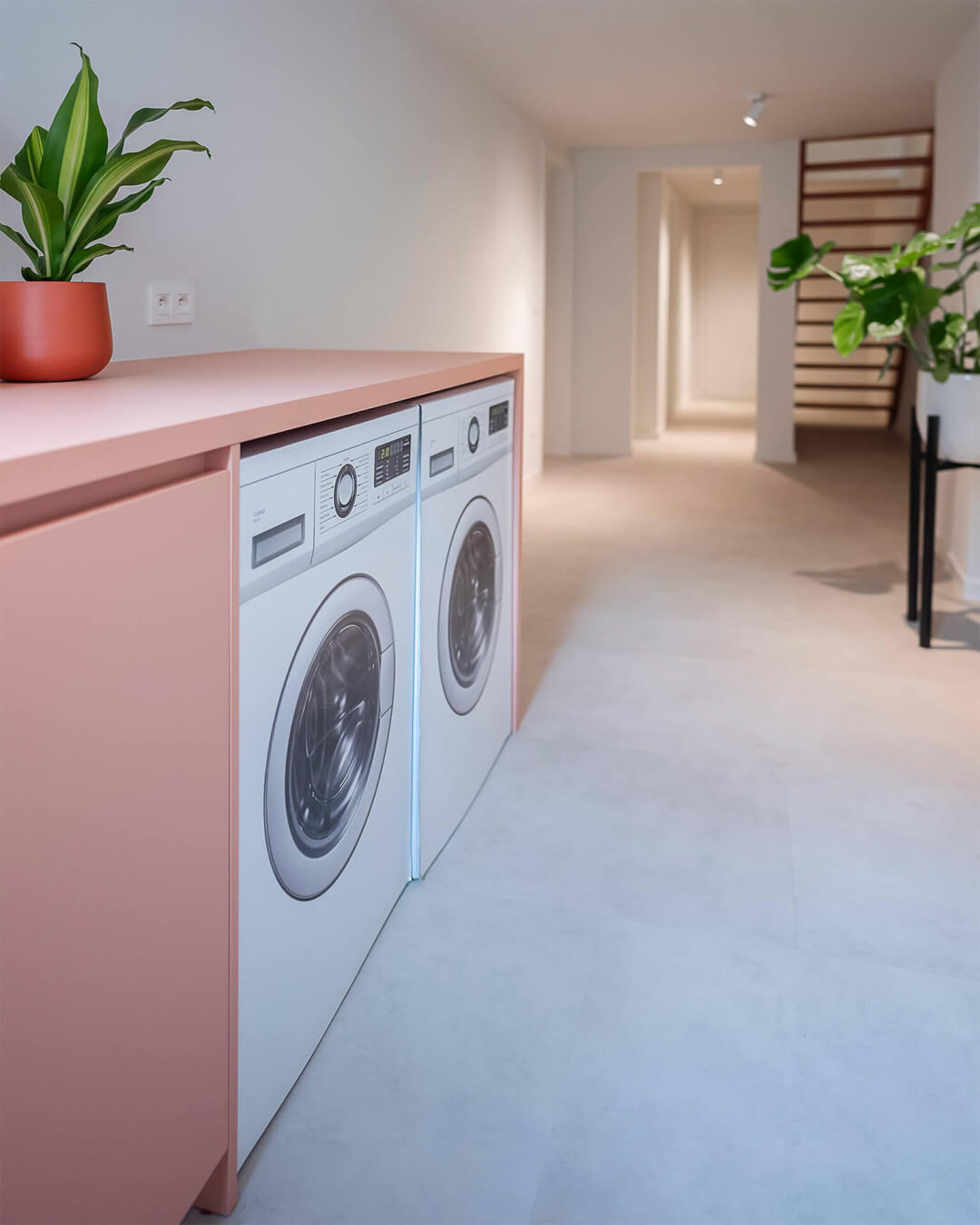 buanderie avec armoires sur mesure comprenant une armoire pour la machine à laver rose et une armoire pour la technologie