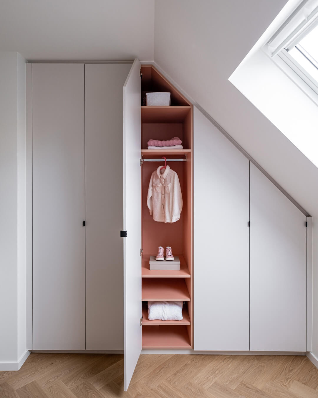Armoire sur mesure sous un toit en pente avec une couleur intérieure rose.