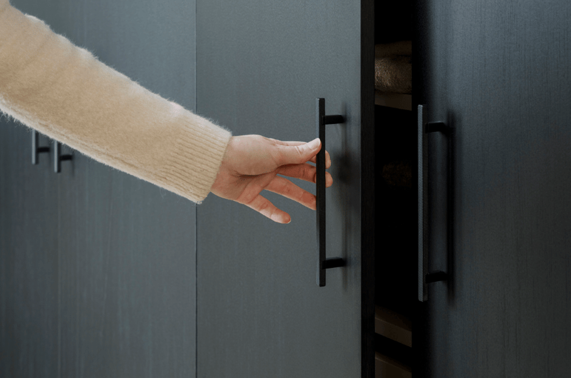Une personne ouvre la porte d'une armoire à l'aide d'une poignée noire.