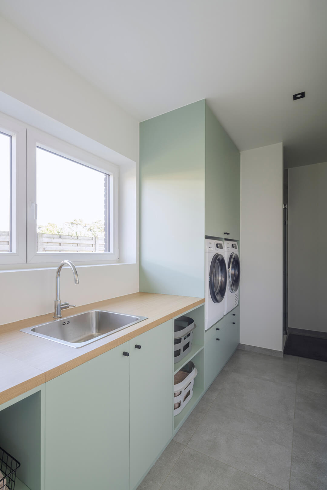 Buanderie aménagée sur mesure en vert industriel avec plan de travail en chêne naturel et lave-linge intégrés