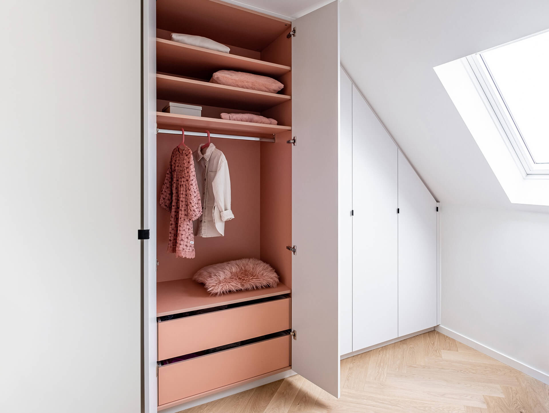 Armoire encastrée sous un toit en pente avec extérieur blanc et intérieur rose