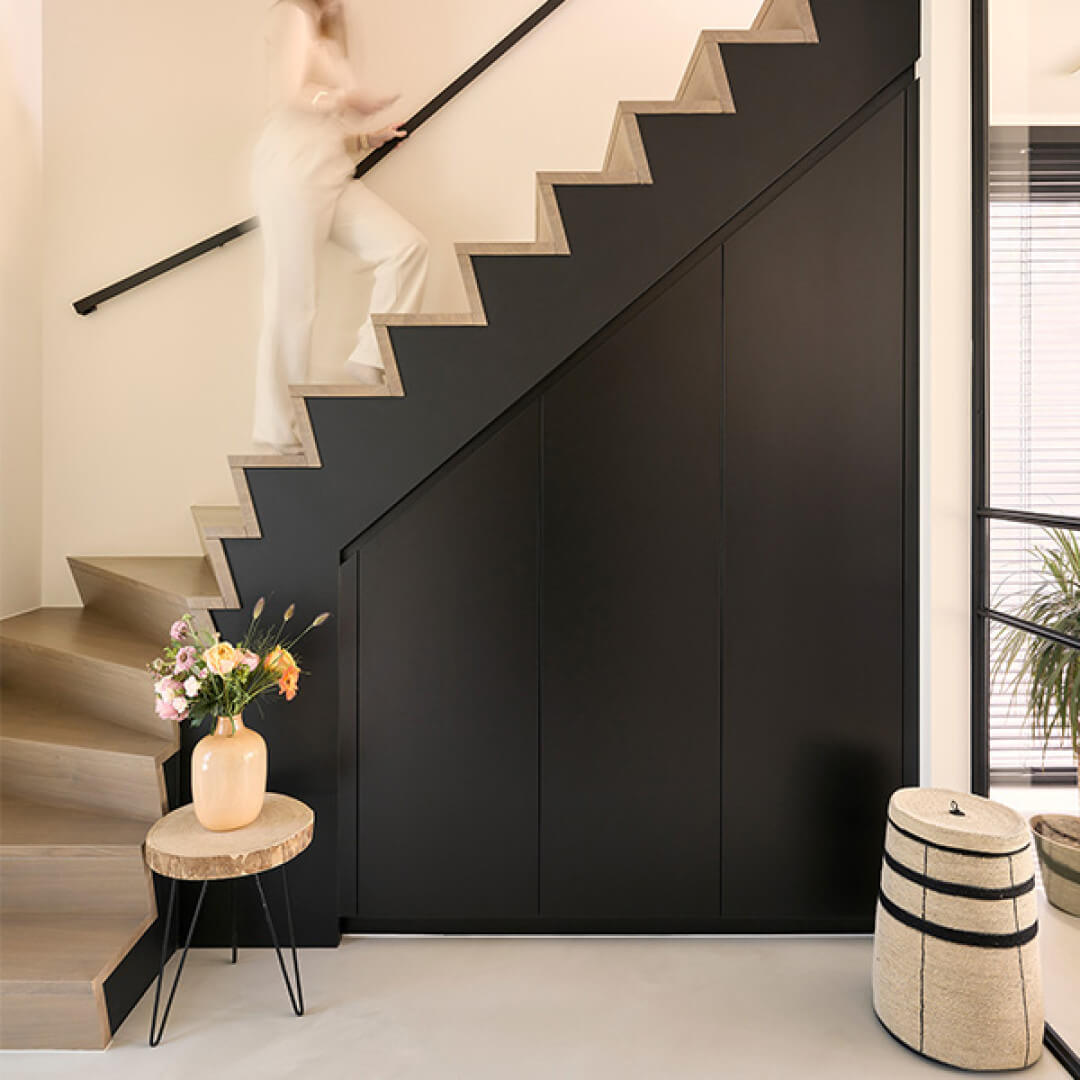 Une femme monte les escaliers ; on aperçoit une armoire sur mesure sous l'escalier.