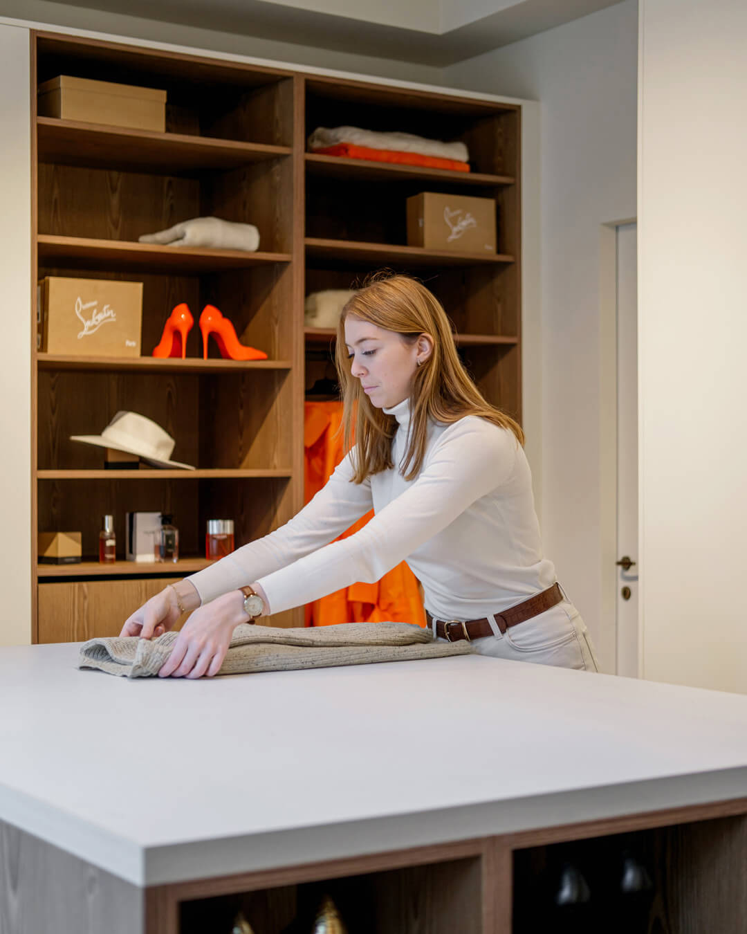 Une femme plie des vêtements sur l'îlot dressing dans la pièce dressing attenante.