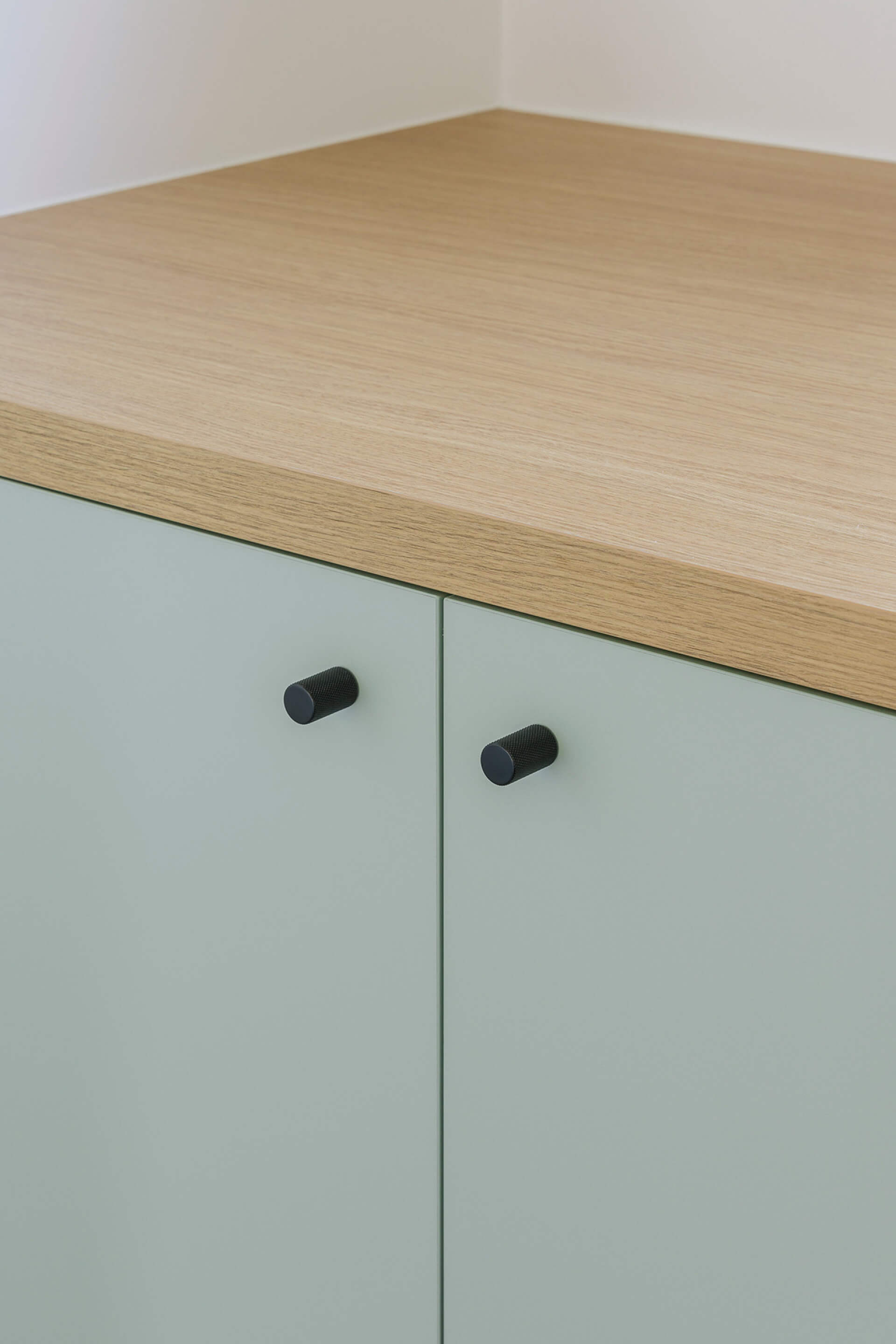 Détail des portes d'armoire vert industriel avec poignée noire et plateau sur mesure en chêne naturel Essential Oak Natural