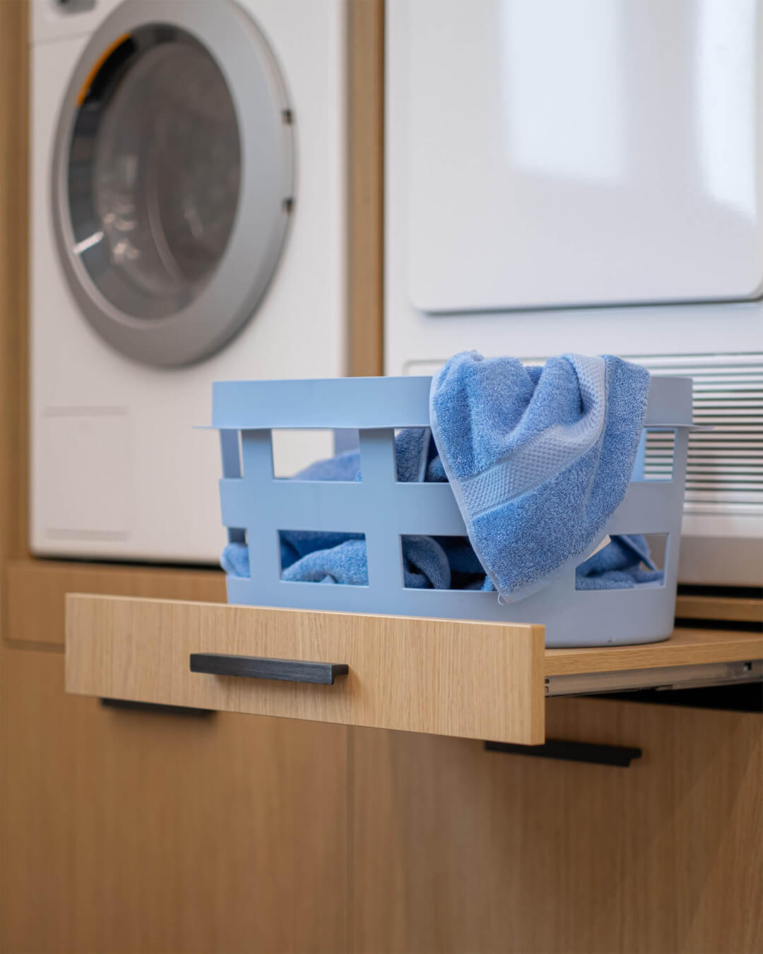 Gros plan d'un panier à linge sur un plateau coulissant sous la machine à laver dans une armoire sur mesure