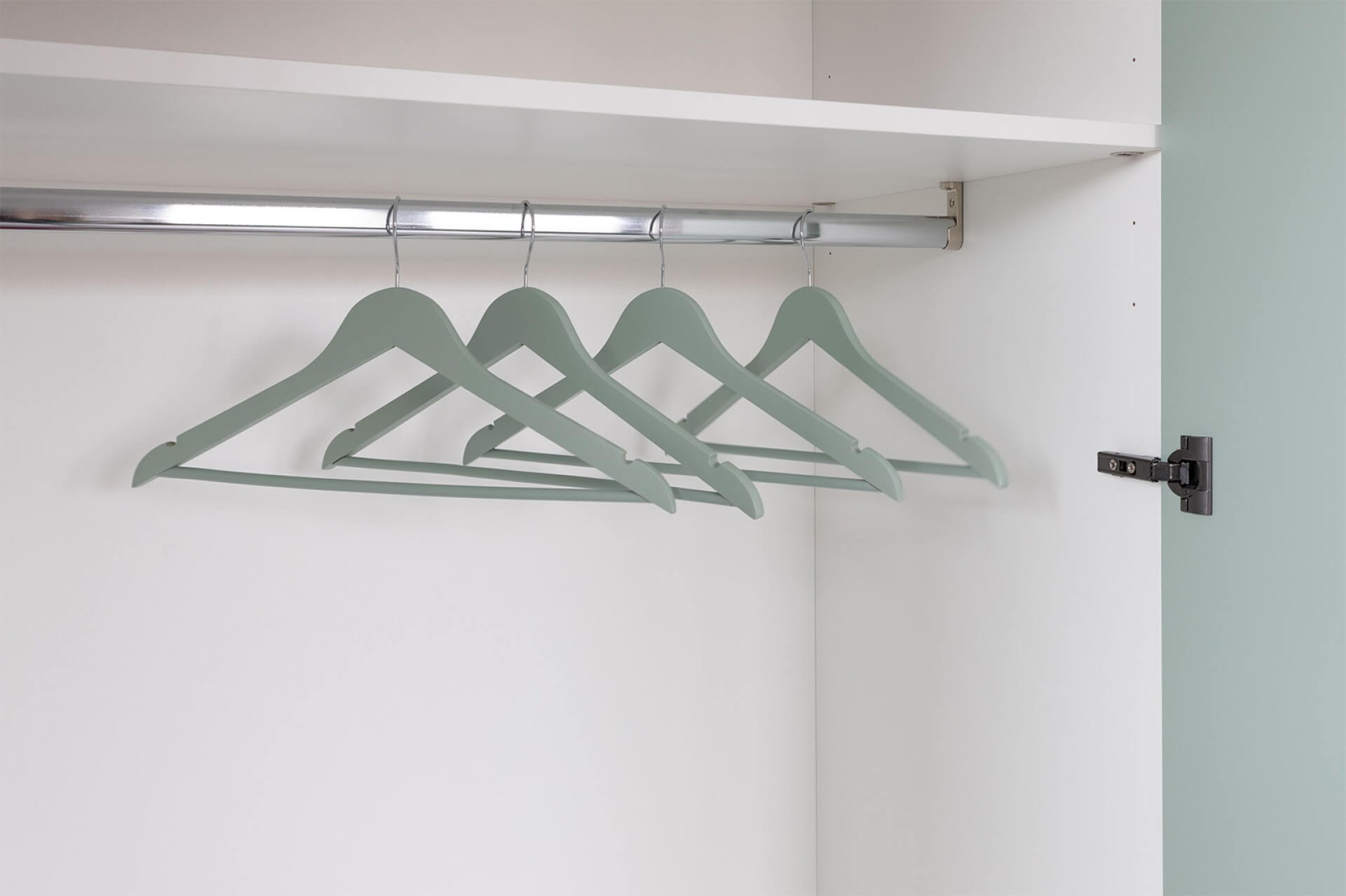 Image d'ambiance de cintres vert industriel suspendus dans une armoire blanche, vide.