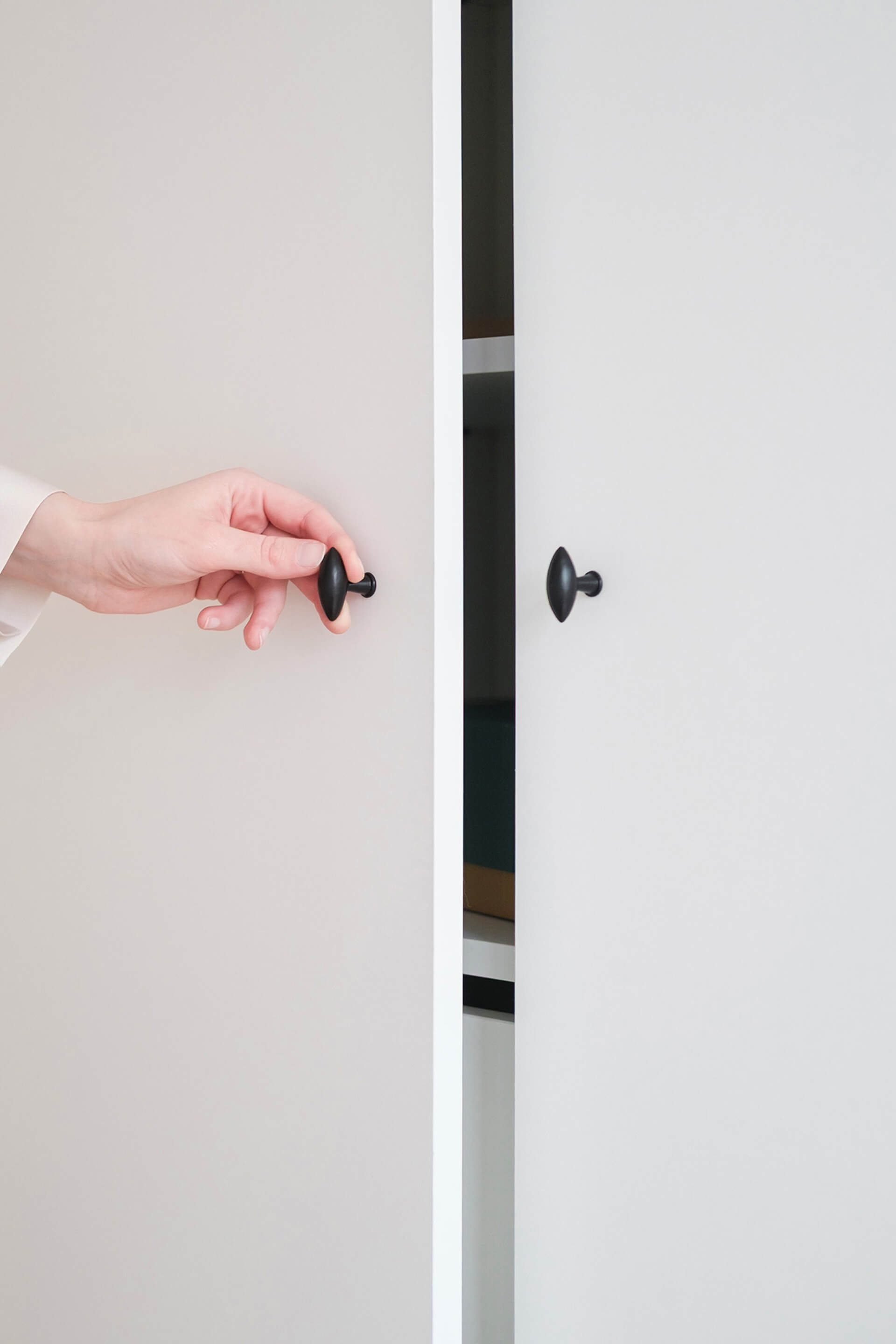 Gros plan sur une armoire blanche munie de poignées noires Olive. Quelqu'un ouvre la porte gauche de l'armoire.
