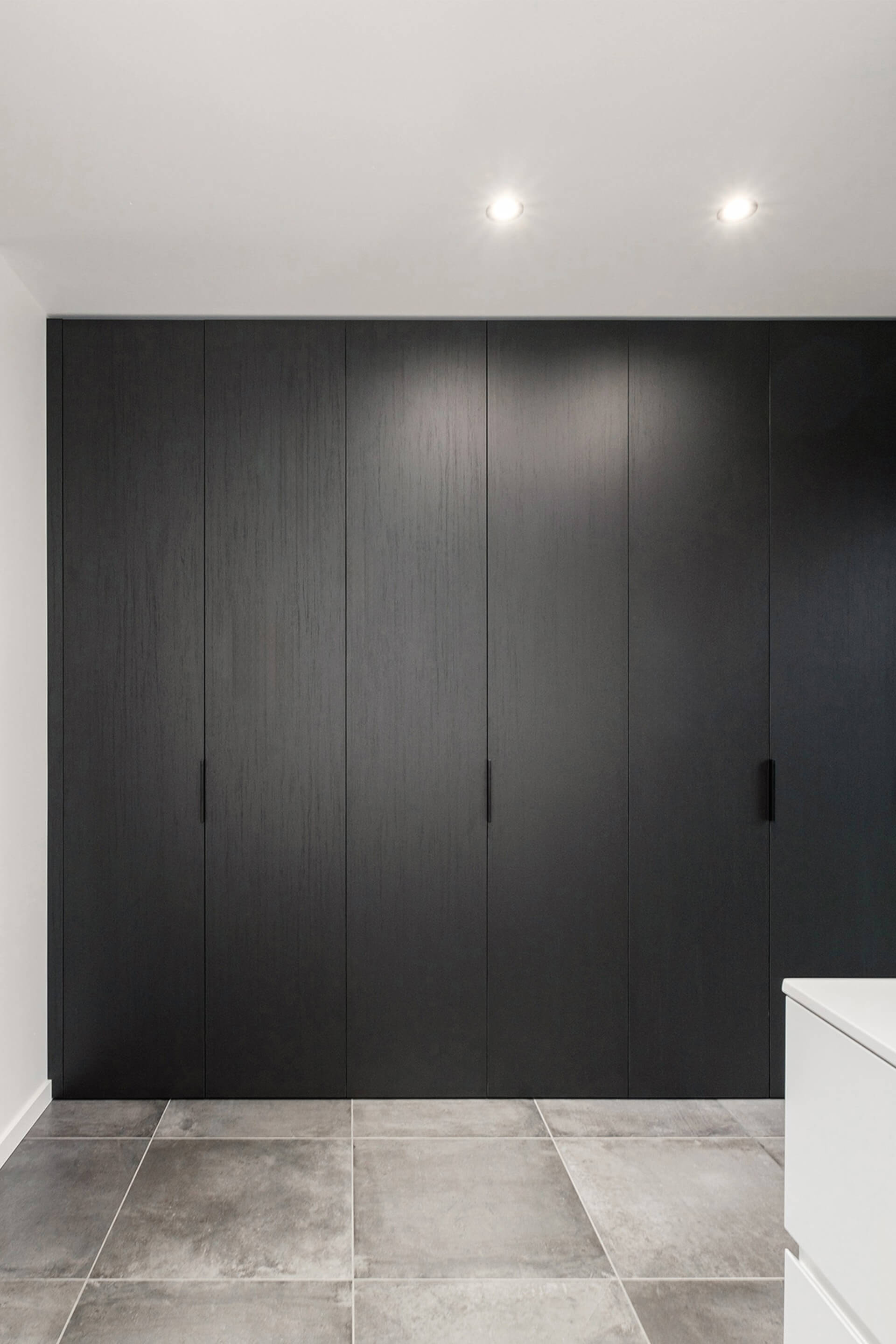 Armoire sur mesure en noir élégant avec poignées Pure noires. L'armoire est fermée ; nous l'observons à quelques mètres de distance afin de bien voir l'ensemble du dressing.