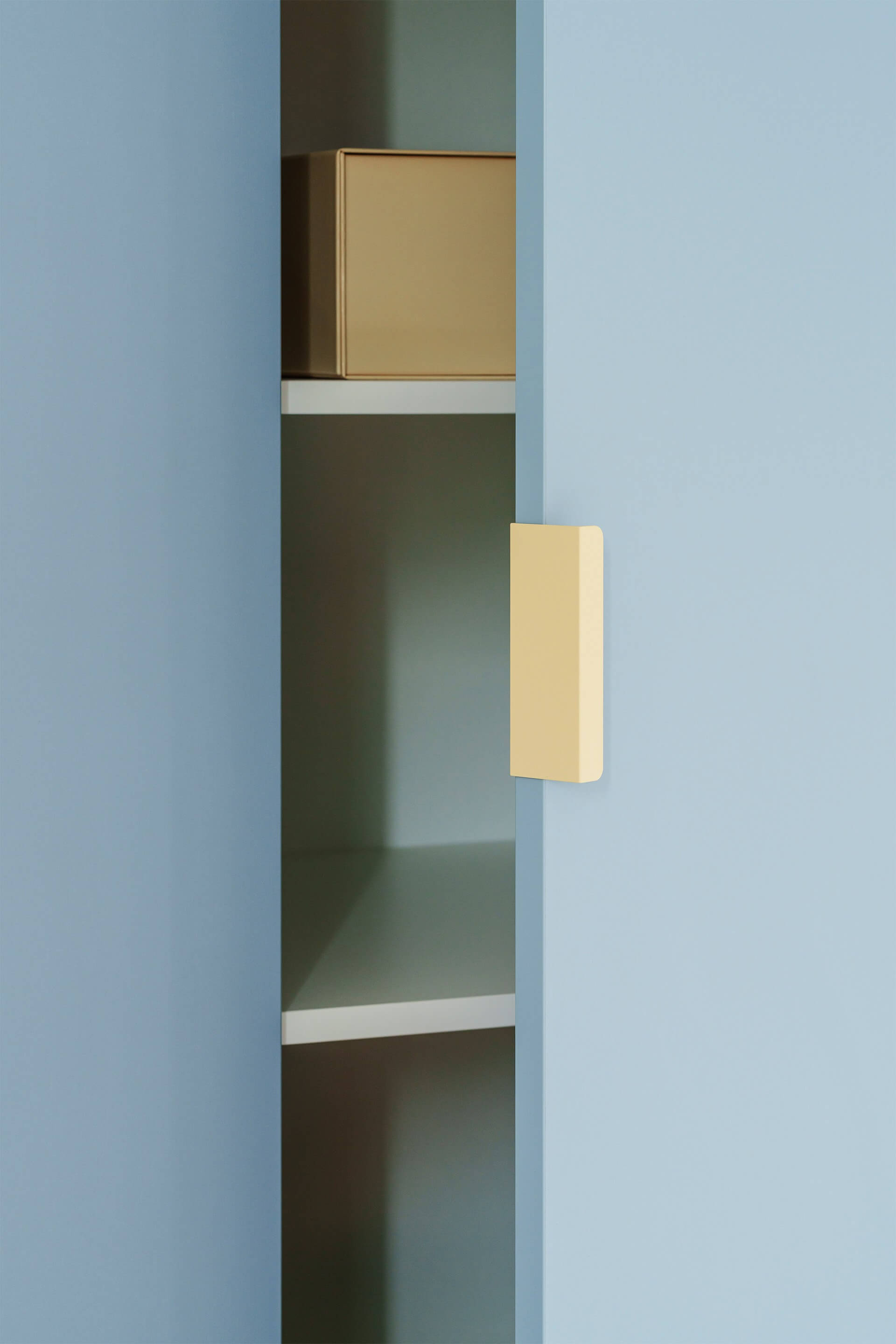 Gros plan sur les poignées Tonton couleur crème montées sur une armoire sur mesure bleu argenté. La porte de l'armoire est entrouverte.