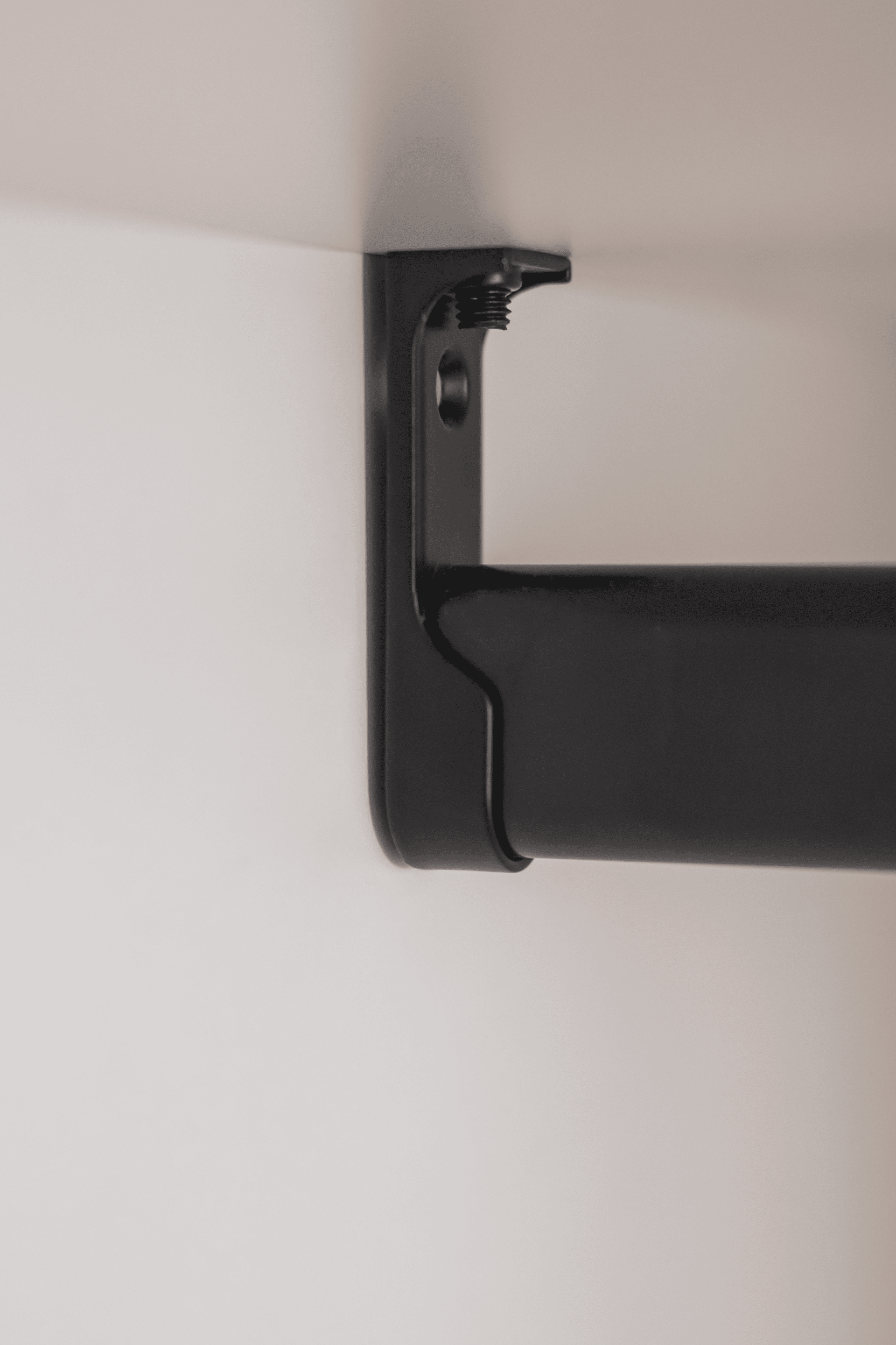 Gros plan sur une tringle à vêtements noire fixée dans une armoire blanche sur mesure. Angle parfait de 90°.